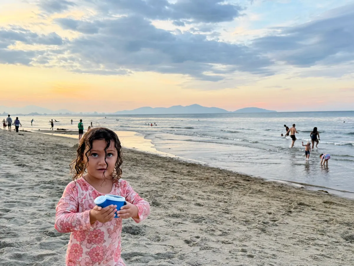 Worldschooling families meet-up at An Bang Beach in Hoi An Vietnam showing children playing in the ocean during sunset with mountains in background