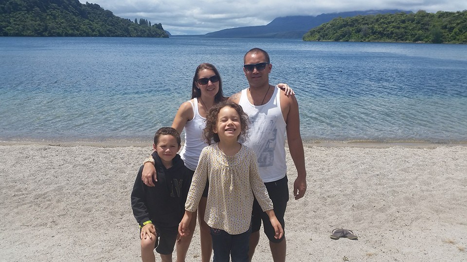 Family of four enjoying a day at Lake Tarawera with clear blue water and green hills in the background