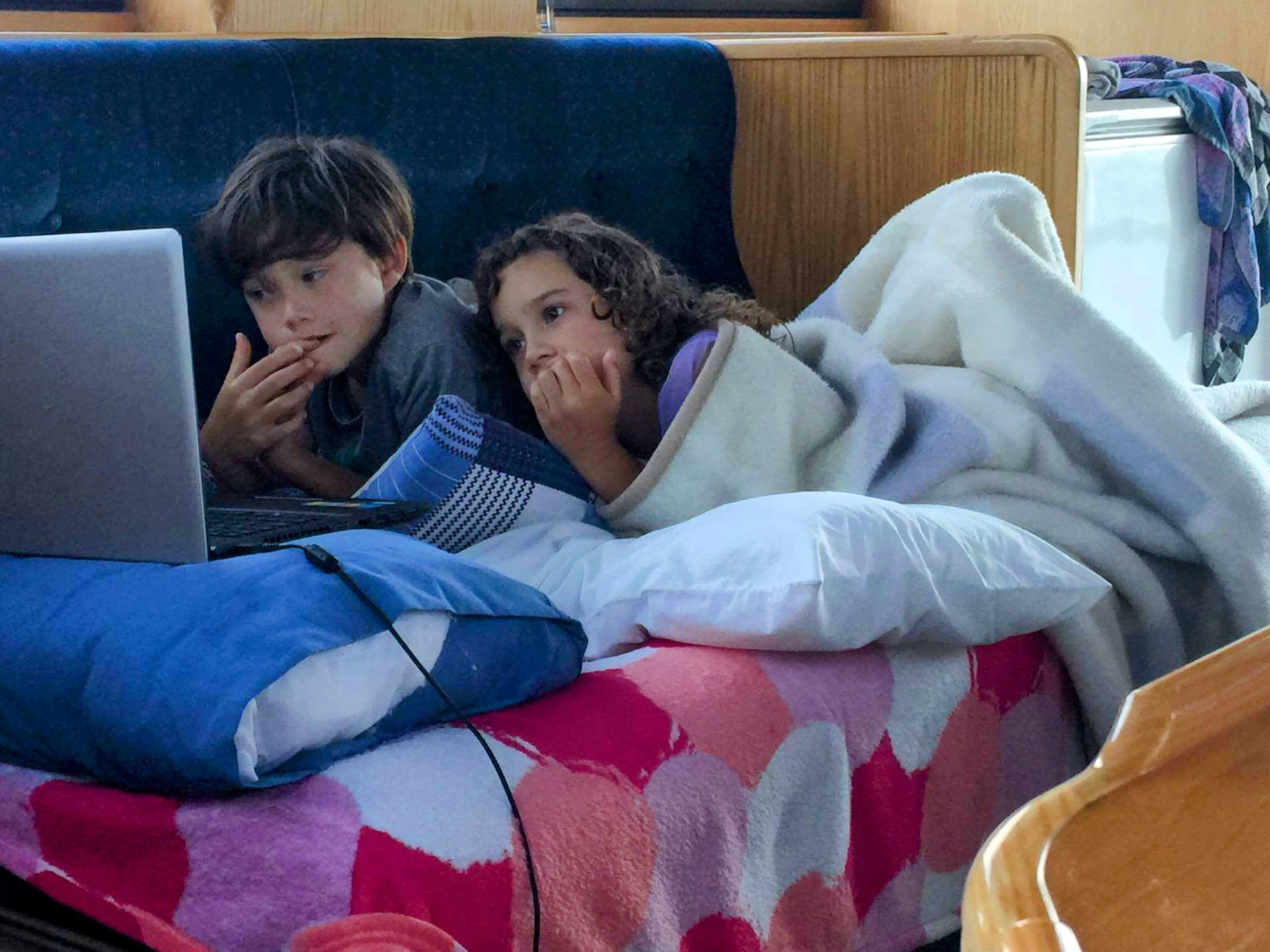 Noah and Aaliyah doing worldschooling lessons on laptop while traveling on a boat in New Zealand